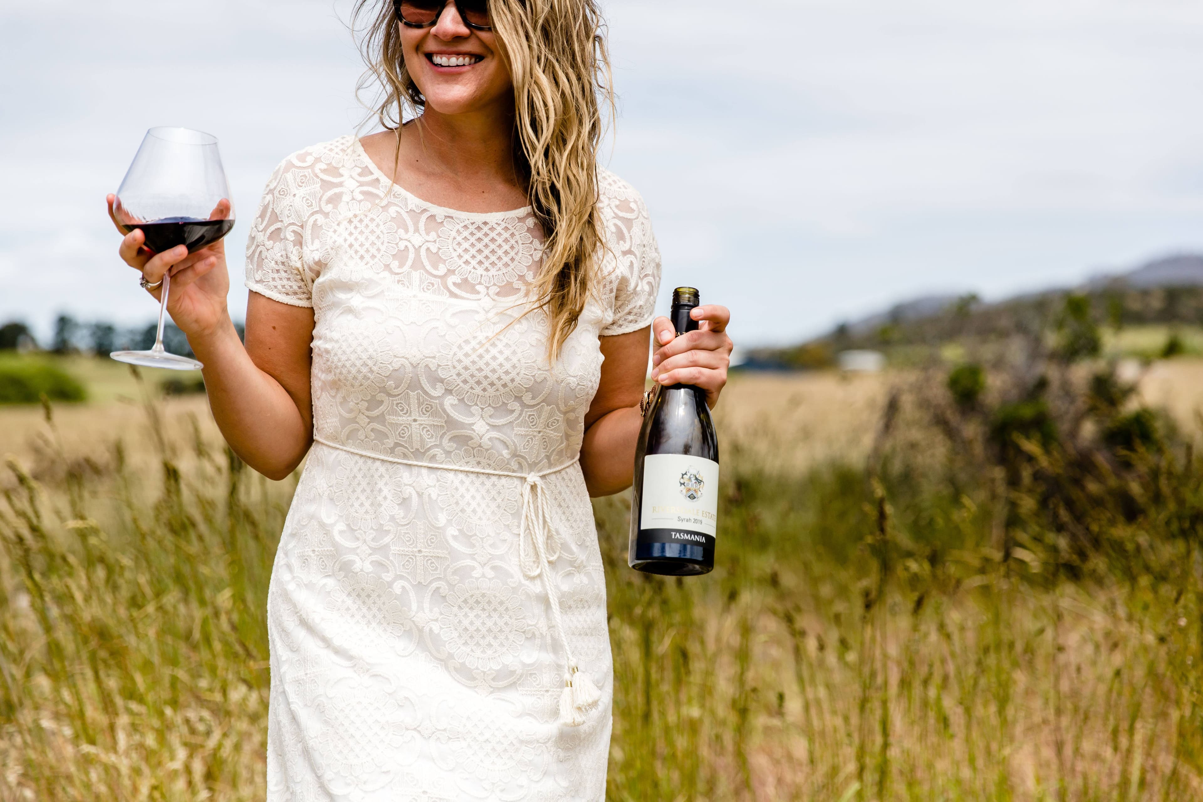 A guest holding a glass of wine and a Riversdale Estate bottle in a vineyard
